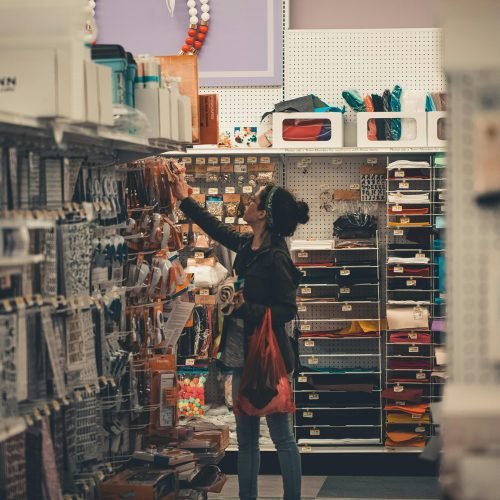 Woman reaching for items in a busy craft store aisle, exploring various art supplies.