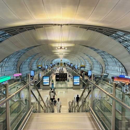 Futuristic architecture of Suvarnabhumi Airport, Bangkok, bustling with travelers.